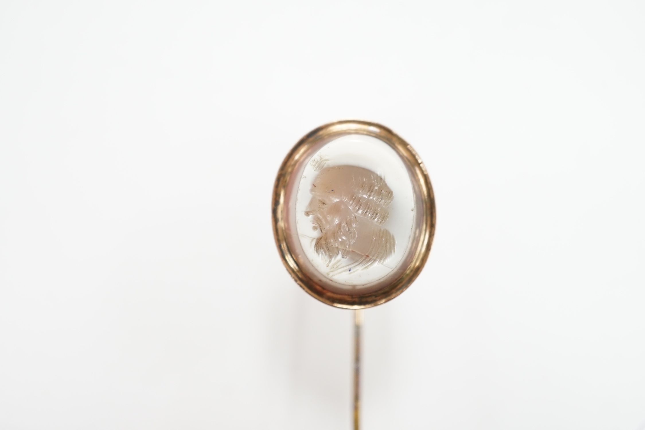 An early 20th century yellow metal and oval intaglio chalcedony set stick pin, 77mm.